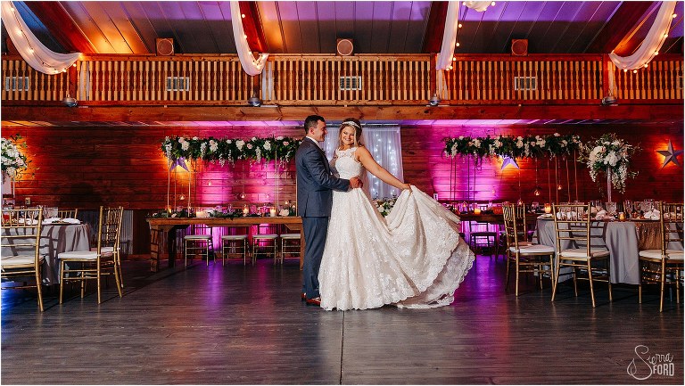 bride flares out wedding gown as groom holds her in reception room at Hidden Barn wedding