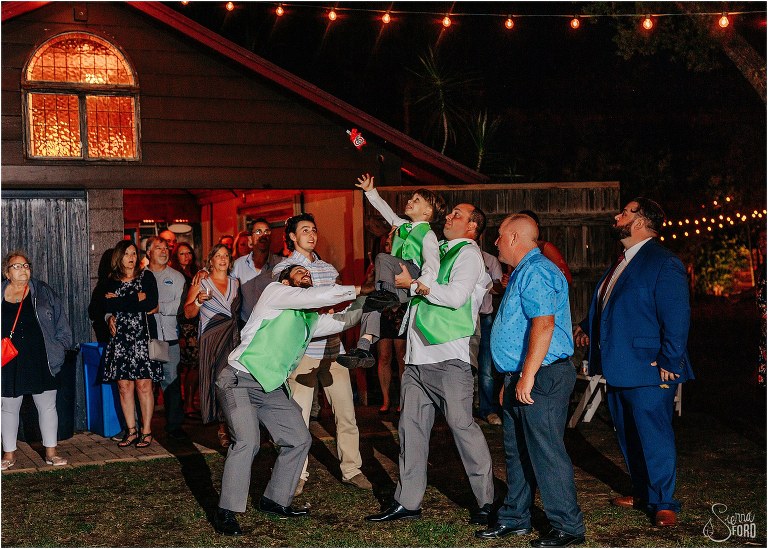 groomsmen lift up ring bearer to catch garter at The Acre Orlando wedding reception