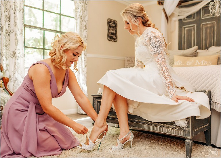 bridesmaid helps bride buckle heels at Bridle Oaks wedding