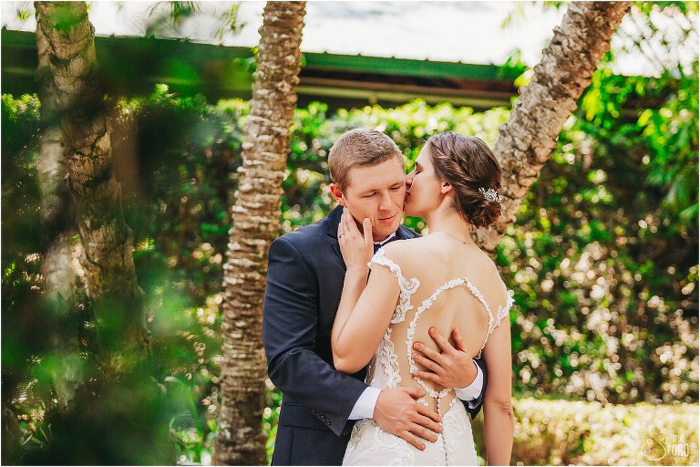 bride kisses groom's cheek gently by palm trees at rustic Apopka wedding