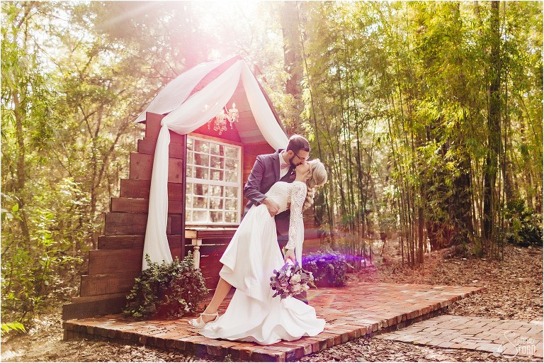 groom dips bride on alter as sun blazes through trees at Bridle Oaks wedding