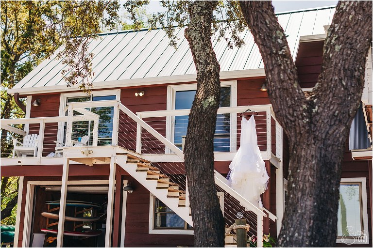 Hailey Paige wedding gown hangs off porch of beach house at Bayfront Lodge wedding