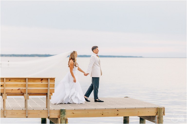 groom leads bride down wooden dock at Bayfront Lodge wedding