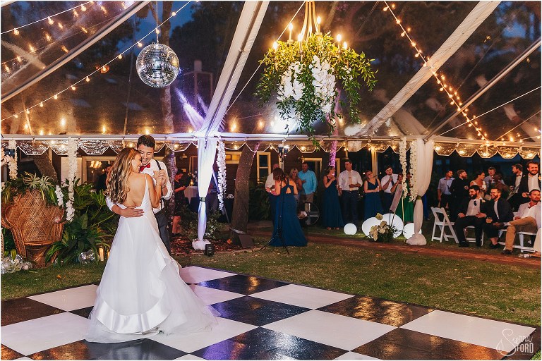 newlyweds share first dance under market lights in clear tent at Bayfront Lodge wedding