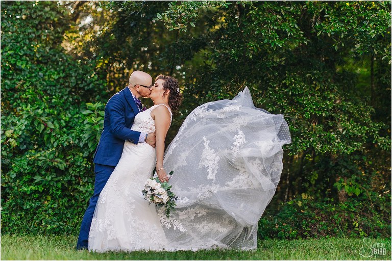 bride's dress blows in wind as groom kisses her at October Oaks wedding
